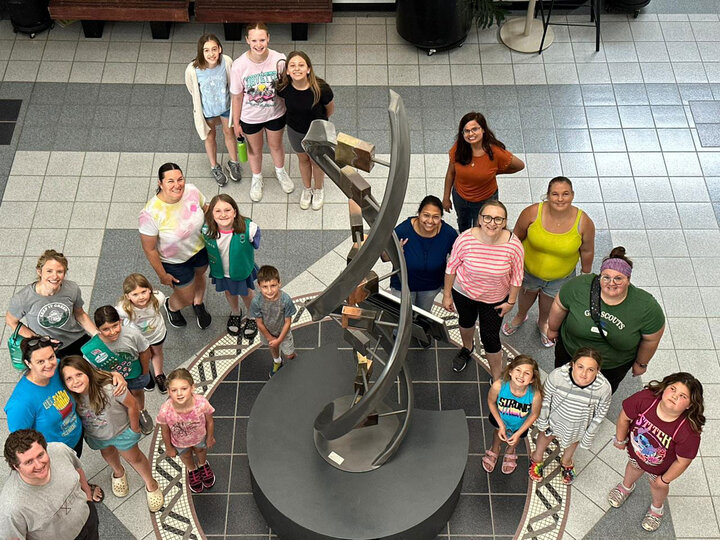 A group of adults and school aged children posing in the atrium of the Beadle Center.